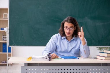 Genç erkek öğretmen yeşil panonun önünde.