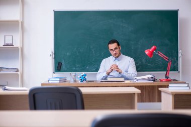 Genç erkek öğretmen yeşil panonun önünde.