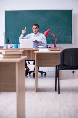 Genç erkek öğretmen yeşil panonun önünde.