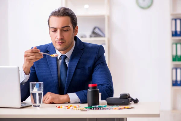 Jonge mannelijke werknemer en veel pillen op het bureau — Stockfoto