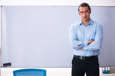 Genç yakışıklı öğretmen beyaz tahtanın önünde.