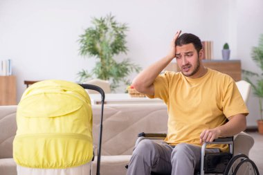 Tekerlekli sandalyede yeni doğan bebeğe bakan genç bir müteahhit.