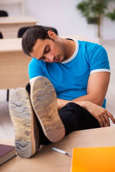 Estudante masculino exausto se preparando para os exames em sala de aula — Fotografia de Stock