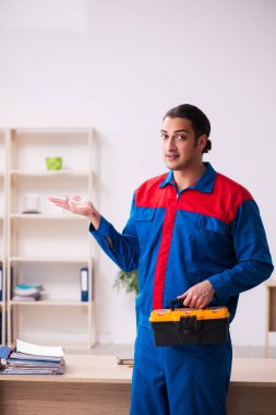 Genç erkek müteahhit ofiste mobilya tamir ediyor.