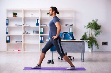 Genç yakışıklı çalışan ofiste spor egzersizleri yapıyor.