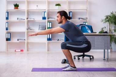 Genç yakışıklı çalışan ofiste spor egzersizleri yapıyor.