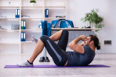 Genç yakışıklı çalışan ofiste spor egzersizleri yapıyor.