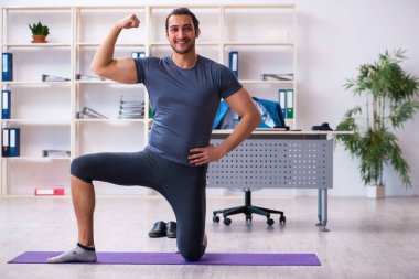 Genç yakışıklı çalışan ofiste spor egzersizleri yapıyor.
