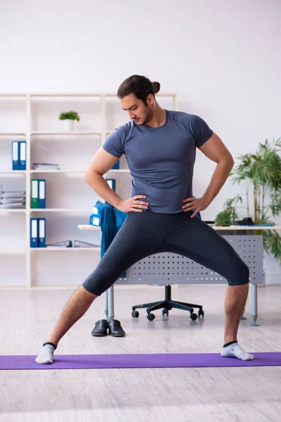 Young handsome employee doing sport exercises in the office