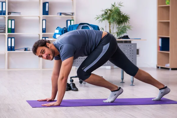 Young handsome employee doing sport exercises in the office