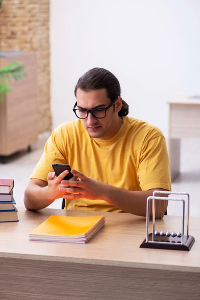 Joven estudiante masculino sosteniendo el teléfono móvil durante la preparación del examen — Foto de Stock