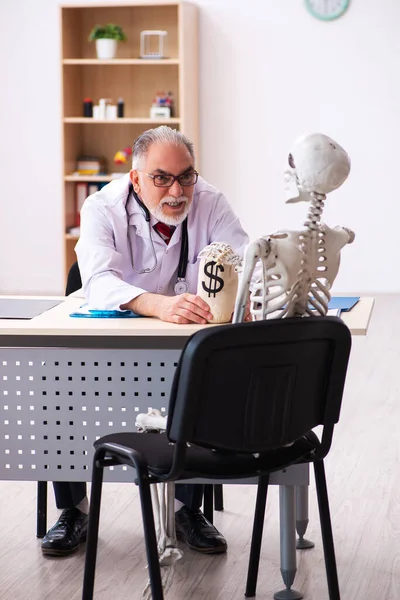 Старый мужчина врач кардиолог и скелет пациента в дорогой м — стоковое фото