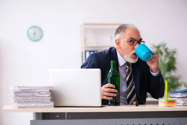 Gammal manlig anställd dricker alkohol på kontoret — Stockfoto
