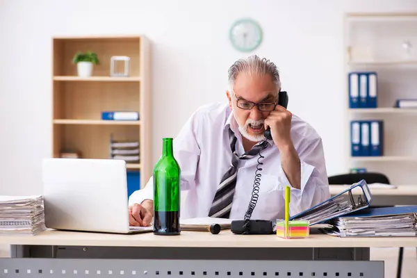 Oude mannelijke werknemer drinkt alcohol op kantoor — Stockfoto