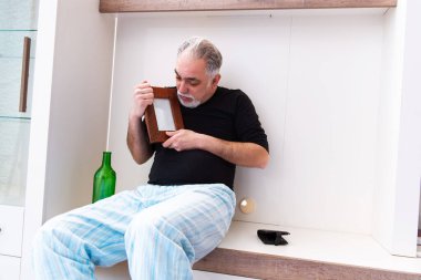 Yaşlı adam yatak odasında şarap içiyor.