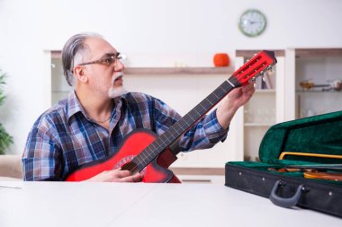 Yaşlı erkek tamirci evde müzik aletlerini tamir ediyor.