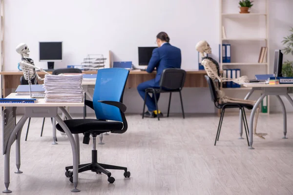 Junge männliche Angestellte mit Skeletten im Büro — Stockfoto