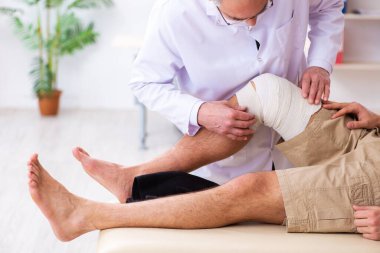 Deneyimli doktor travmatolog genç erkek hastayı muayene ediyor.