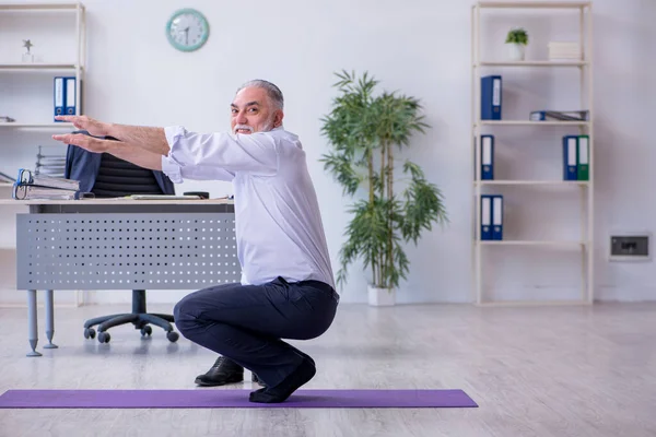 Aged male employee doing physical exercises during break — Stock Photo, Image