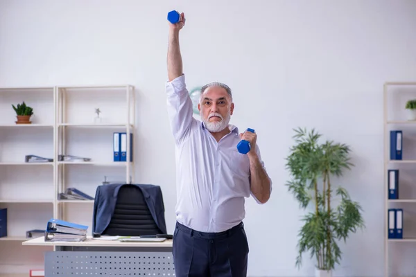 Verouderde mannelijke werknemer doet fysieke oefeningen tijdens de pauze — Stockfoto