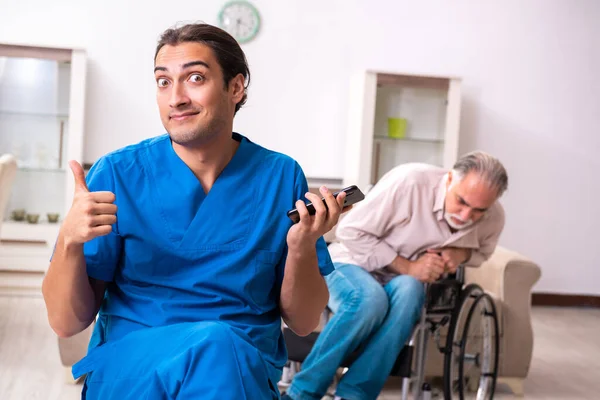Старик в инвалидной коляске и молодой плохой сиделка в помещении — стоковое фото
