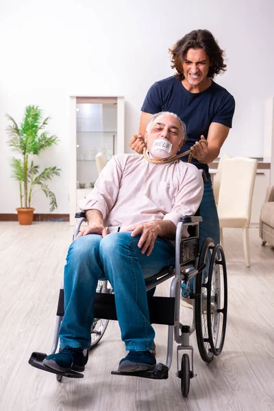 Oude man in rolstoel en jonge slechte verzorger binnen — Stockfoto