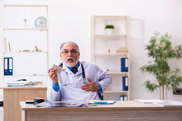 Velho médico do sexo masculino que escreve prescrição na clínica — Fotografia de Stock