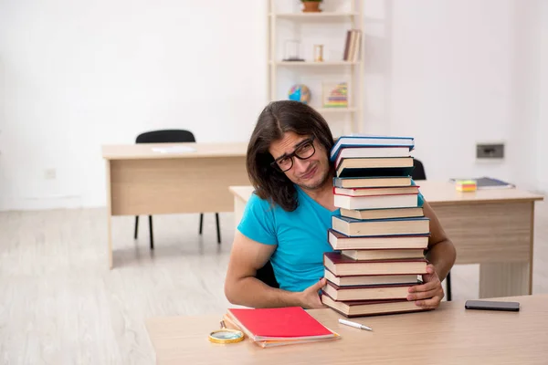 Jovem estudante do sexo masculino e um monte de livros na classe — Fotografia de Stock