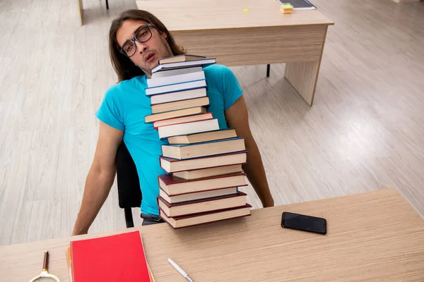 Ung manlig student och många böcker i klassen — Stockfoto