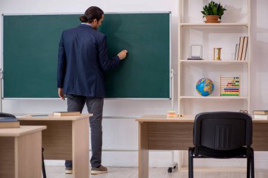 Genç erkek öğretmen yeşil panonun önünde.