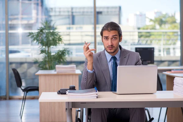 Jonge mannelijke werknemer in rolstoel werkzaam in het kantoor — Stockfoto