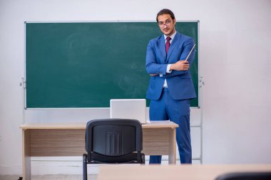 Yeşil panonun önünde takım elbiseli genç bir öğretmen.