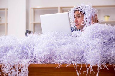 Genç bir erkek çalışan ve ofiste bir sürü kesik kağıt var.