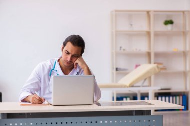 Genç erkek doktor klinikte not alıyor.