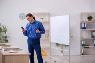 Genç erkek öğretmen ders sırasında elinde akıllı telefon tutuyor.