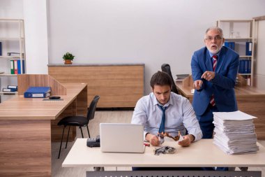 Genç erkek çalışan ve yaşlı patron iş yerinde kağıtları yakıyor.