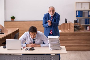 Genç erkek çalışan ve yaşlı patron iş yerinde kağıtları yakıyor.