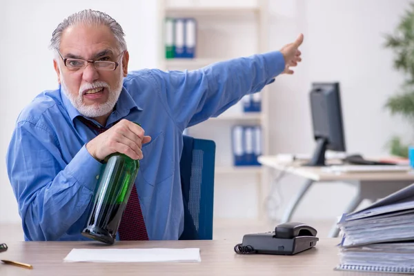 Oude mannelijke werknemer drinkt alcohol op kantoor — Stockfoto