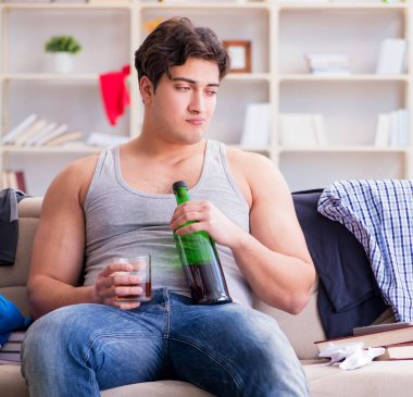 Dağınık bir odada alkol alan genç bir öğrenci.