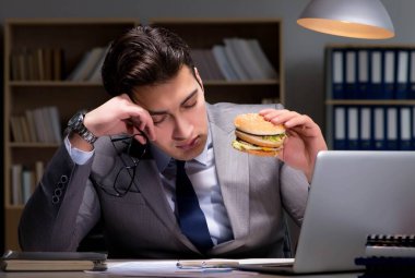 Gece geç saatte iş adamı hamburger yiyor.