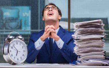 Yığınla evrak işi ve alarm sistemi olan bir iş adamı.