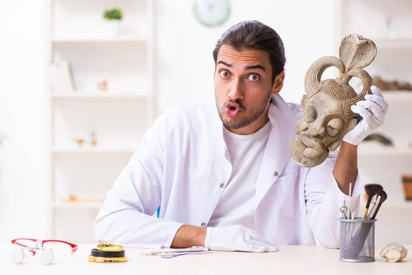 Jonge mannelijke archeoloog bestudeert het oude Afrikaanse steenmasker — Stockfoto