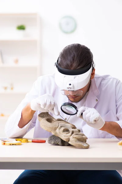 Jonge mannelijke archeoloog bestudeert het oude Afrikaanse steenmasker — Stockfoto