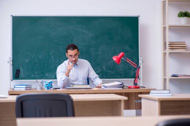 Genç erkek öğretmen yeşil panonun önünde.