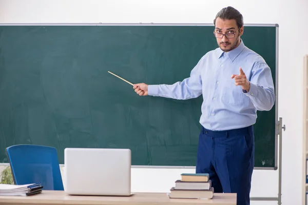 Fiatal férfi tanár az osztályteremben a zöld tábla előtt — Stock Fotó