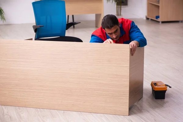 Young male contractor repairing furniture in the office