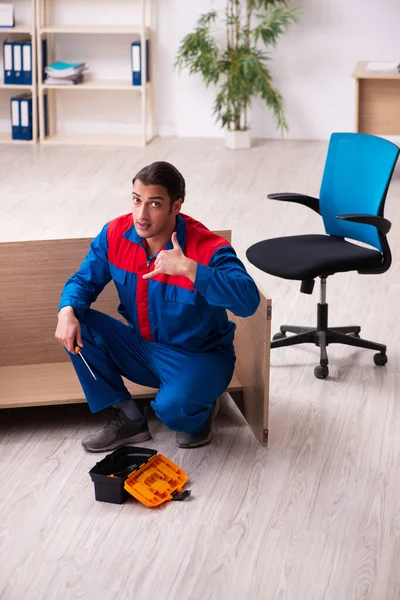 Jovem empreiteiro do sexo masculino reparando móveis no escritório — Fotografia de Stock