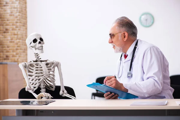 Старый врач и пациент со скелетом в клинике — стоковое фото
