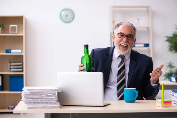 Старый работник-мужчина пьет алкоголь в офисе — стоковое фото
