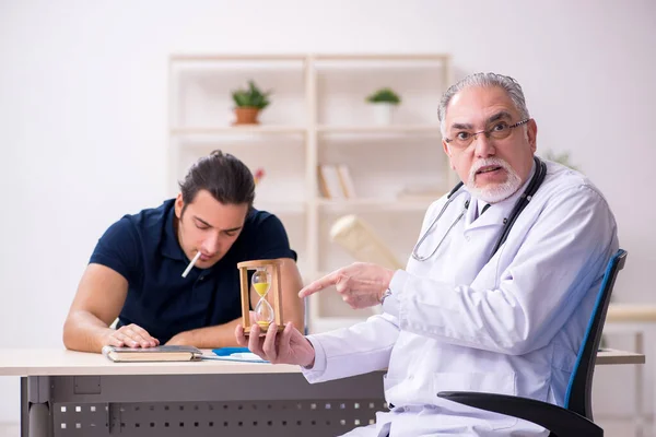 Молодой пациент мужского пола посещает старого врача в концепции антисмокинга — стоковое фото